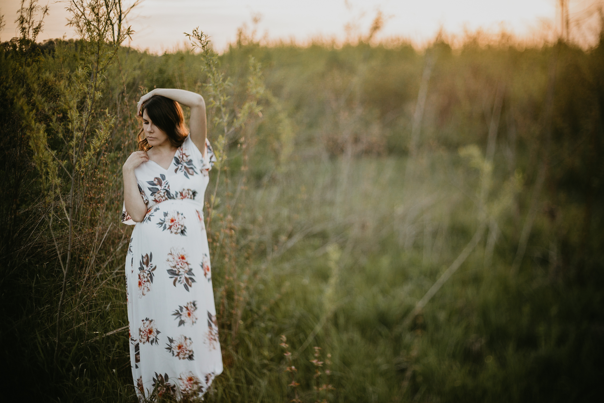 Expecting woman with her arms raised in a golden field of grasses.